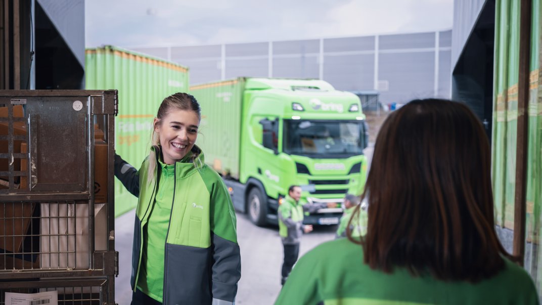Woman holds container with parcels in front of a truck
