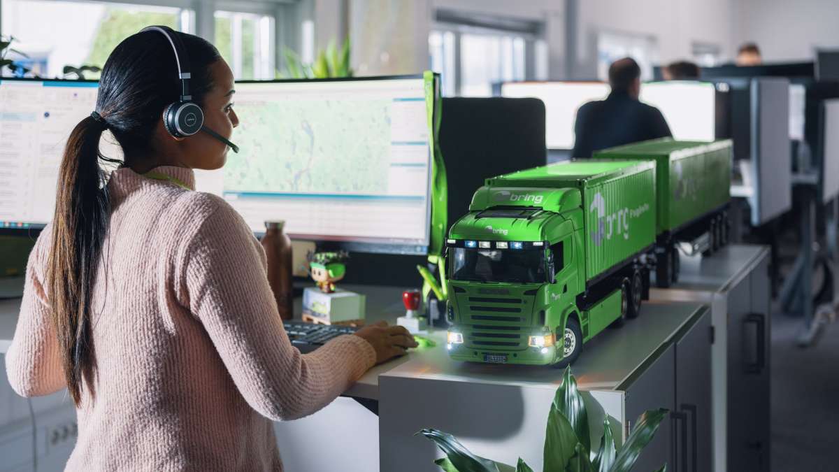 En ansatt ved Brings kundeservice står foran en datamaskin med headset på.