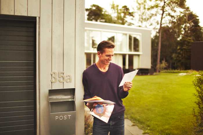 En mann som står ved siden av en postkasse og ser på reklamene han har fått