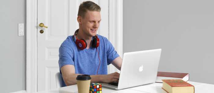 En mann med røde hodetelefoner rundt halsen som ser på en laptop