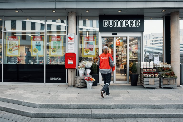 Ett Postenbud går utenfor en butikk for å levere en pakke