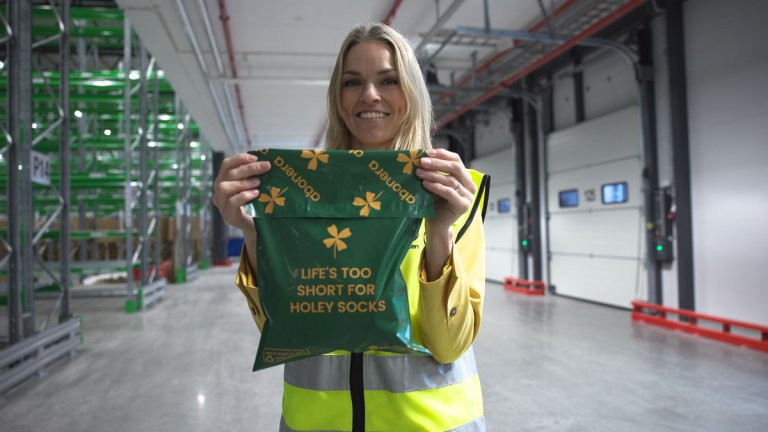 Dame som står inne på et lager og holder en grønn pose